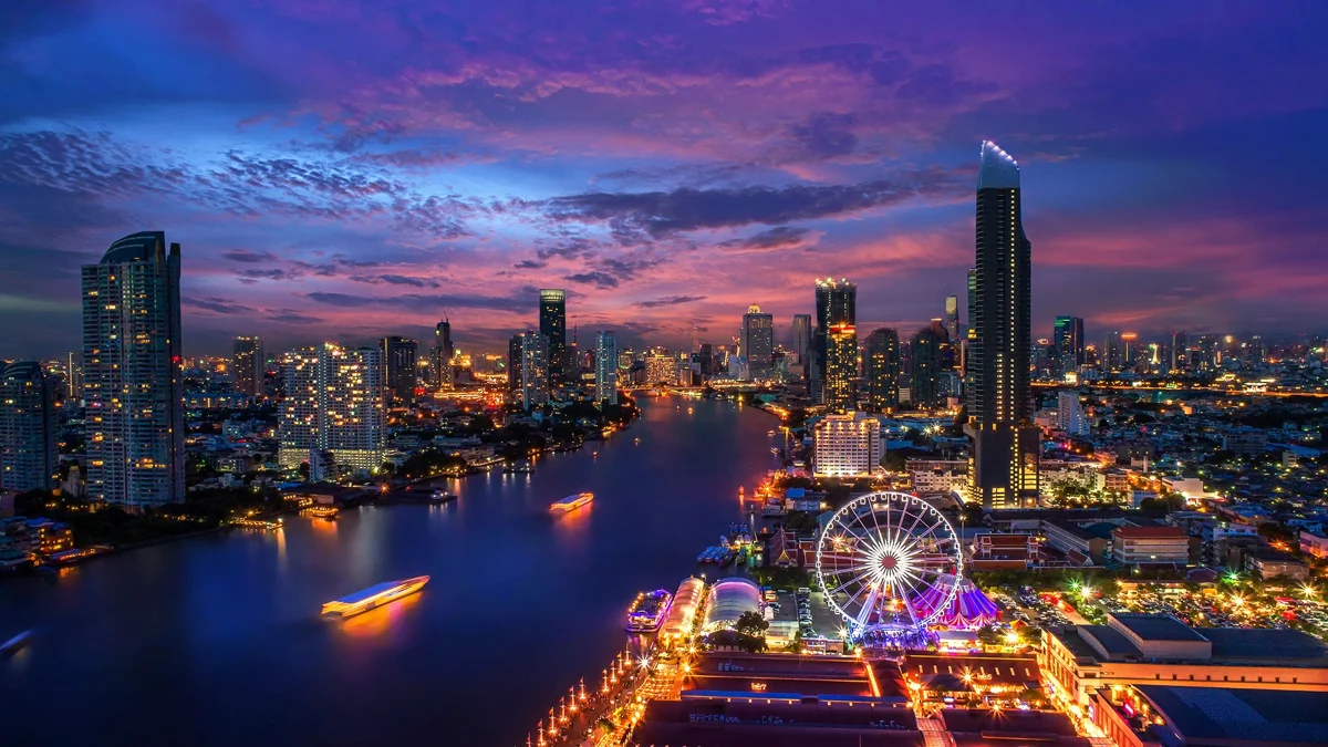 Night view of Bangkok skyline along the Chao Phraya River with illuminated skyscrapers and Ferris wheel.