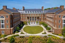 Modern university campus with red brick academic buildings surrounding a circular green courtyard.