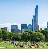 A sunny day at Central Park in New York City with people relaxing on the grass and skyscrapers in the background.