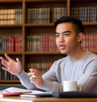 A student speaking and gesturing during a discussion in a library setting.