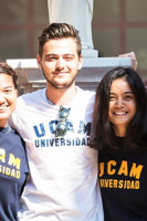 Students smiling and wearing UCAM Universidad shirts outdoors on campus.