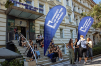 Students gathering outside the University of New York in Prague entrance, sitting on steps and socializing near blue university banners.